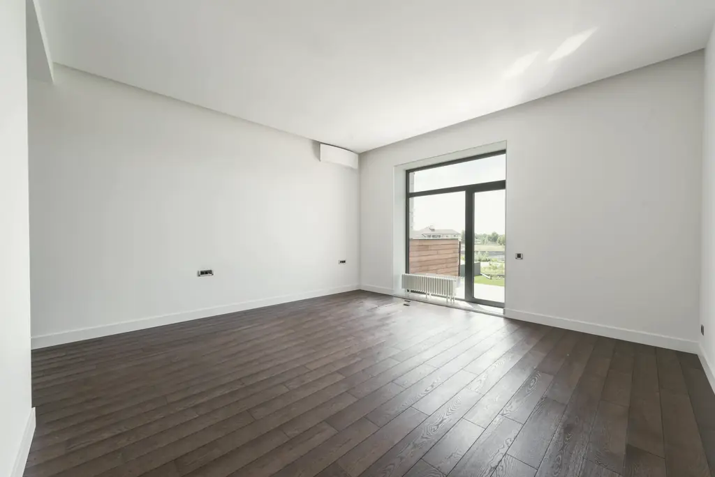 Leerer, heller Raum mit weißen Wänden, dunklem Parkett und Balkontür nach der Räumung.