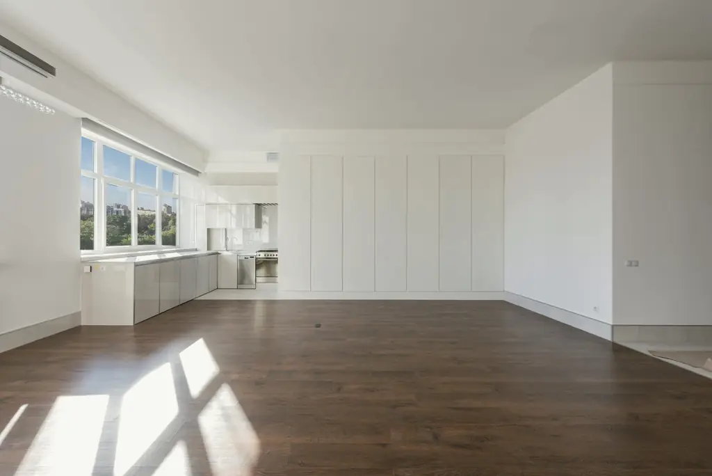 Leere, helle Wohnung mit dunklem Holzboden, auf den Sonnenlicht durch große Fenster fällt.